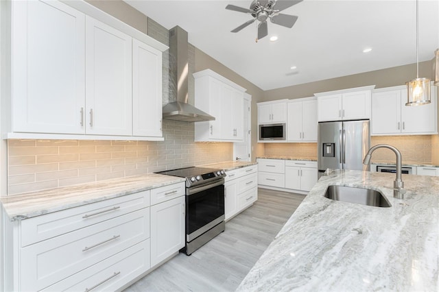 kitchen featuring sink, wall chimney exhaust hood, decorative light fixtures, white cabinetry, and stainless steel appliances