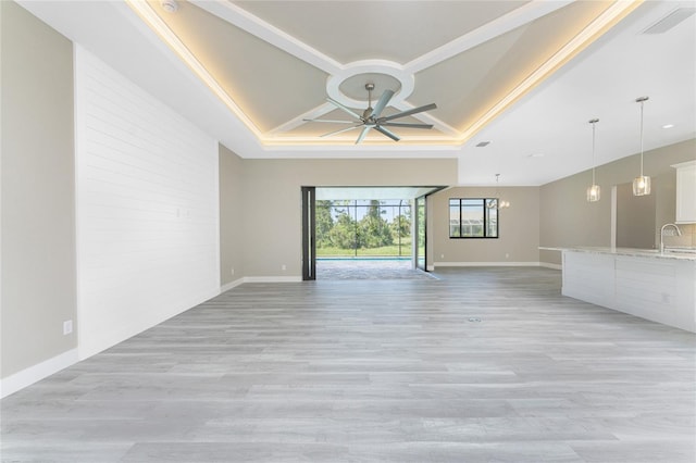 unfurnished living room featuring a raised ceiling, ceiling fan, sink, and light wood-type flooring