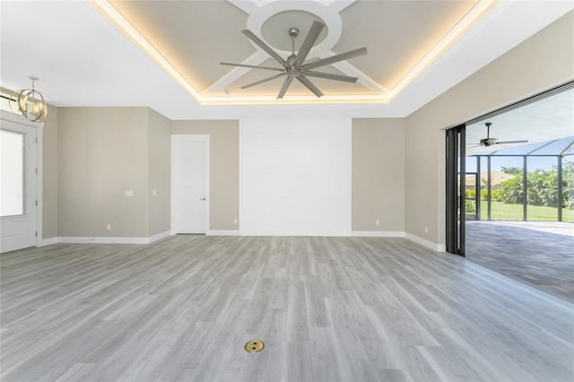 unfurnished living room featuring a tray ceiling, crown molding, light hardwood / wood-style flooring, and ceiling fan with notable chandelier