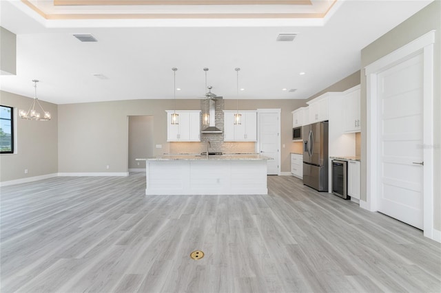 kitchen featuring stainless steel appliances, wall chimney range hood, pendant lighting, light hardwood / wood-style floors, and white cabinetry