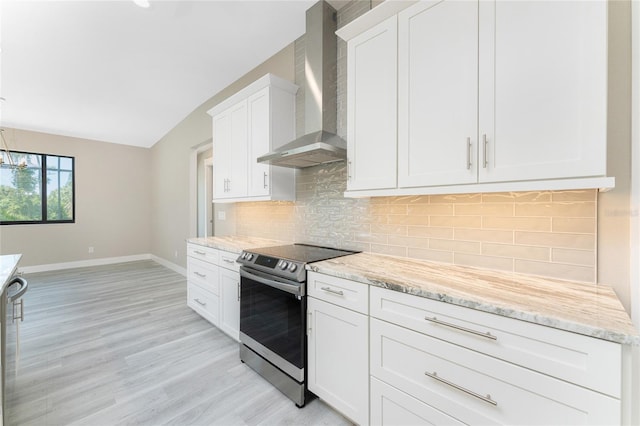 kitchen with light stone counters, wall chimney exhaust hood, stainless steel electric stove, white cabinets, and light hardwood / wood-style floors