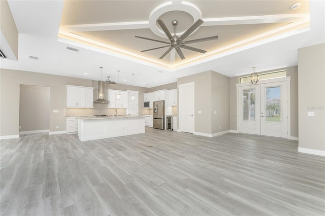 unfurnished living room featuring french doors, ceiling fan with notable chandelier, light hardwood / wood-style floors, and a raised ceiling