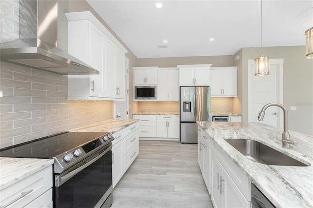 kitchen featuring sink, wall chimney exhaust hood, tasteful backsplash, light hardwood / wood-style floors, and appliances with stainless steel finishes