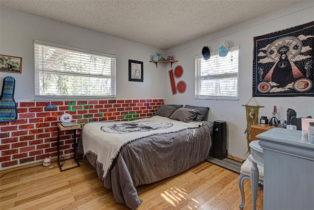 bedroom featuring light wood-type flooring, a textured ceiling, brick wall, and multiple windows