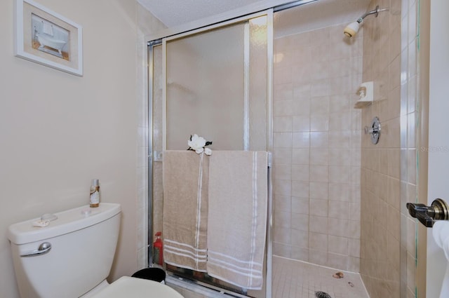 bathroom featuring a textured ceiling, toilet, and a shower with door