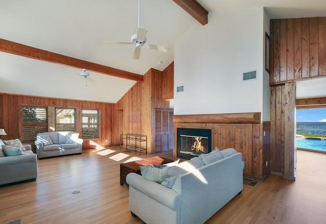 living room with beam ceiling, light hardwood / wood-style floors, high vaulted ceiling, and wood walls