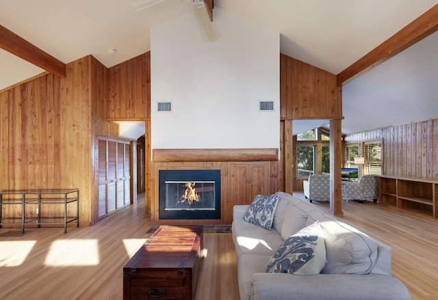 living room featuring wood walls, light hardwood / wood-style flooring, beamed ceiling, and high vaulted ceiling