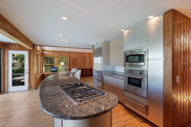 kitchen featuring built in appliances, a kitchen island with sink, and wooden walls