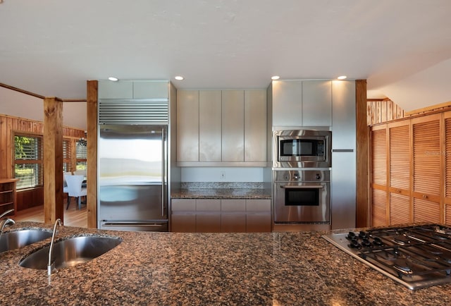 kitchen featuring built in appliances, dark stone counters, and sink