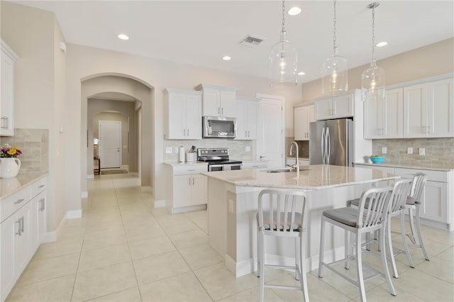 kitchen featuring a center island with sink, sink, stainless steel appliances, white cabinets, and hanging light fixtures