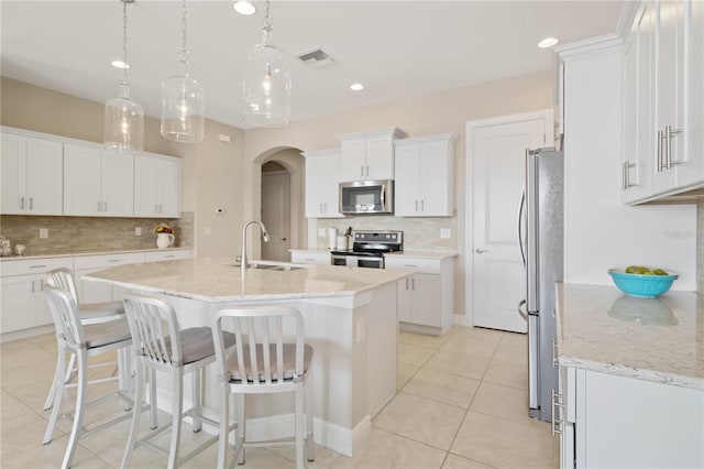 kitchen featuring a center island with sink, stainless steel appliances, decorative light fixtures, sink, and white cabinets