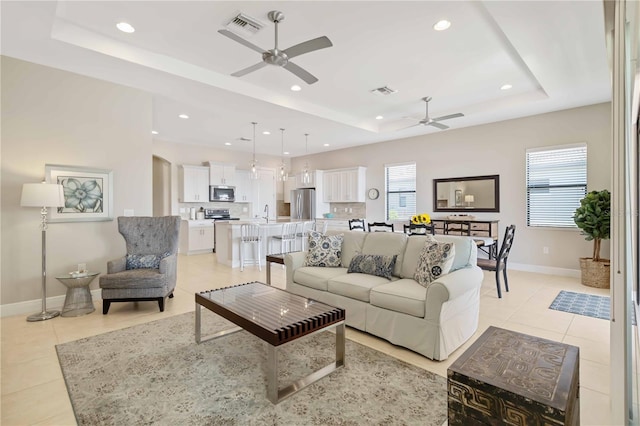 living room featuring a tray ceiling, ceiling fan, and light tile patterned flooring