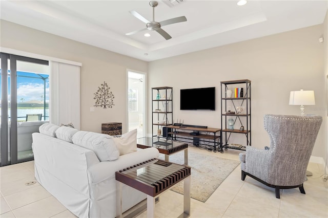 tiled living room with ceiling fan and a raised ceiling