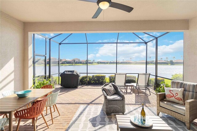 view of patio / terrace featuring grilling area, a water view, ceiling fan, and glass enclosure