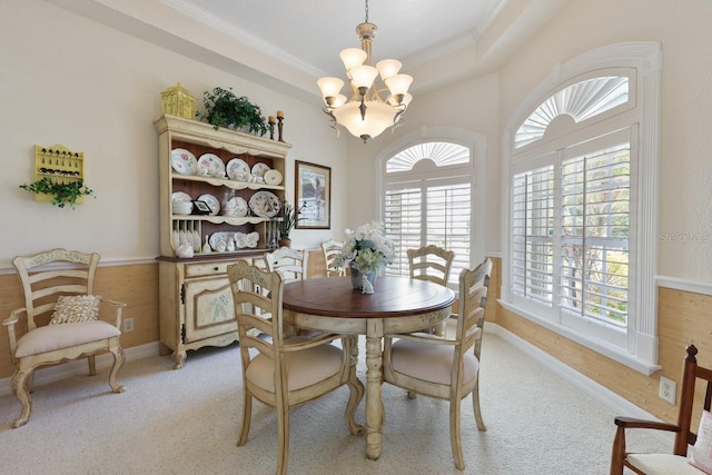 carpeted dining area with ornamental molding, a raised ceiling, and a chandelier