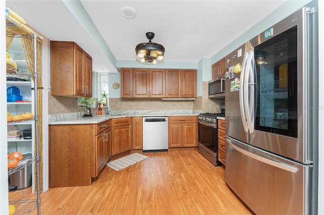 kitchen with tasteful backsplash, light stone countertops, stainless steel appliances, and light hardwood / wood-style floors