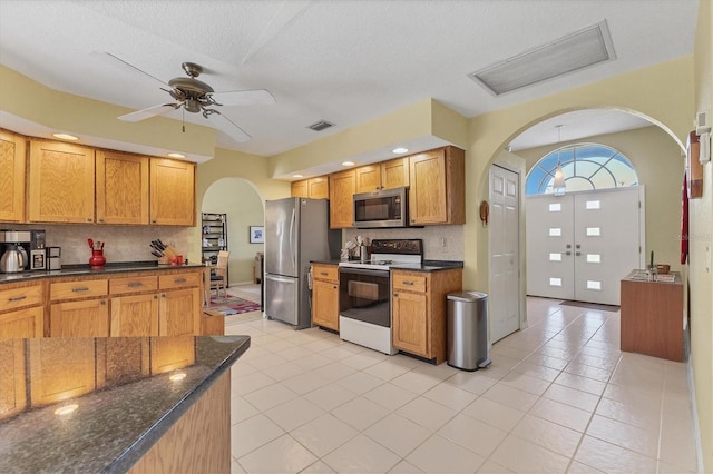 kitchen with ceiling fan, dark stone countertops, decorative backsplash, light tile patterned floors, and appliances with stainless steel finishes