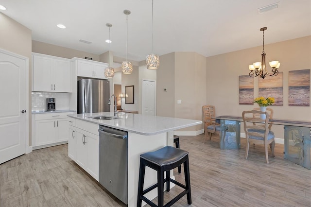 kitchen featuring stainless steel appliances, sink, decorative light fixtures, white cabinetry, and an island with sink