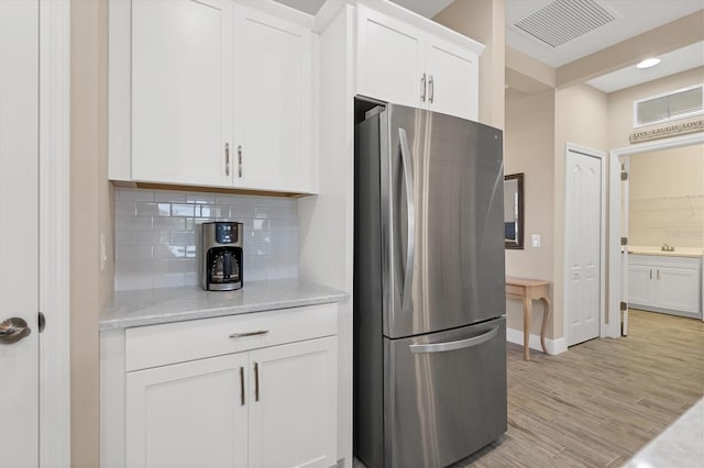 kitchen featuring decorative backsplash, light stone counters, light hardwood / wood-style floors, white cabinetry, and stainless steel refrigerator