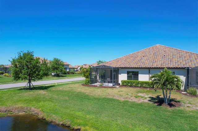 back of house with glass enclosure, a water view, and a yard