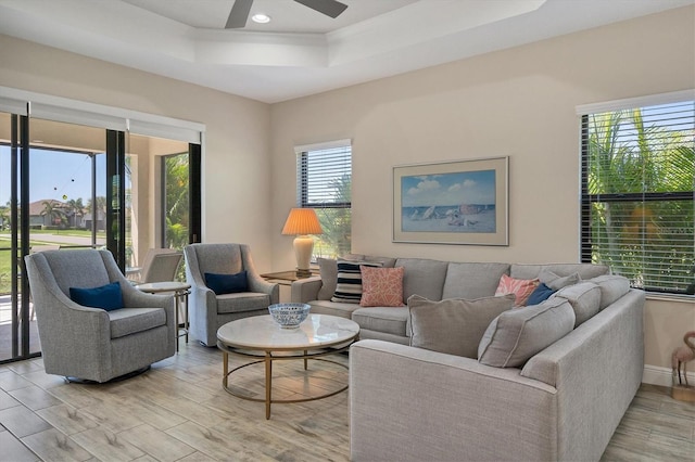 living room featuring a raised ceiling, a wealth of natural light, ceiling fan, and light hardwood / wood-style floors