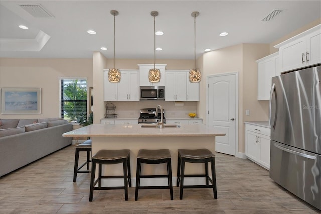 kitchen featuring decorative light fixtures, stainless steel appliances, a center island with sink, and sink