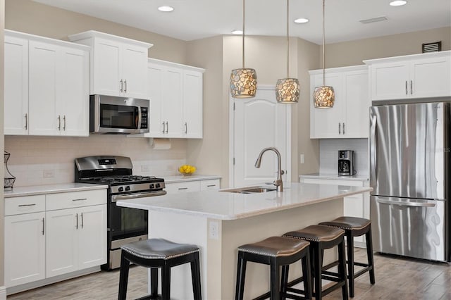 kitchen with white cabinets, appliances with stainless steel finishes, decorative light fixtures, and an island with sink