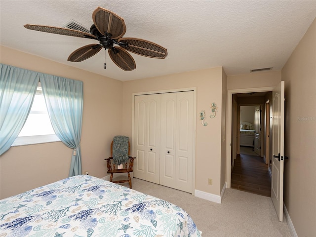 bedroom with ceiling fan, a closet, light carpet, and a textured ceiling