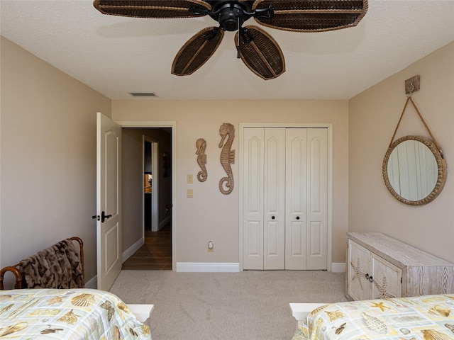 bedroom featuring ceiling fan, a closet, light colored carpet, and a textured ceiling