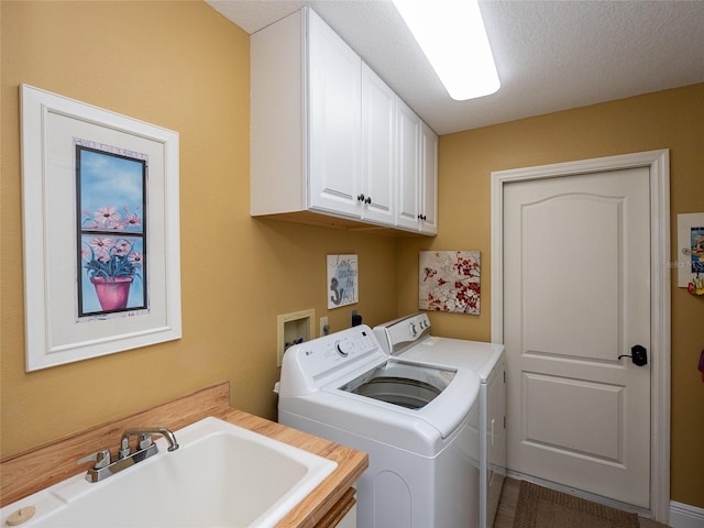 clothes washing area with cabinets, a textured ceiling, sink, and washing machine and clothes dryer