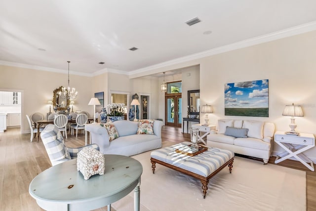 living room featuring french doors, light hardwood / wood-style floors, ornamental molding, and a notable chandelier