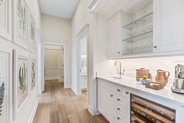 bar with white cabinetry, light hardwood / wood-style flooring, beverage cooler, and sink