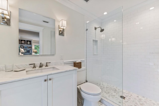 bathroom featuring vanity, toilet, ornamental molding, and tiled shower