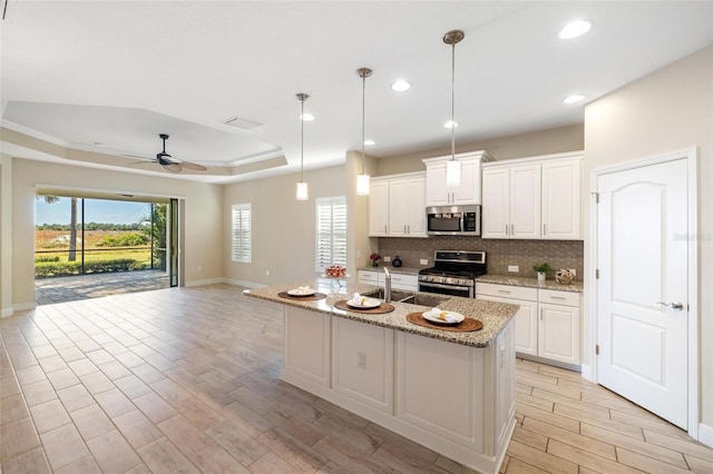 kitchen with a center island with sink, ceiling fan, white cabinetry, and stainless steel appliances