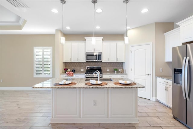 kitchen with white cabinetry, stainless steel appliances, light stone counters, an island with sink, and pendant lighting