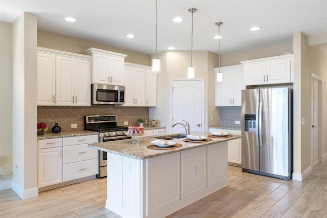 kitchen with white cabinets, a center island with sink, light stone countertops, and stainless steel appliances