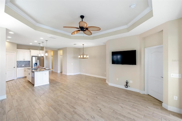 kitchen featuring a raised ceiling, a kitchen island with sink, decorative light fixtures, and appliances with stainless steel finishes