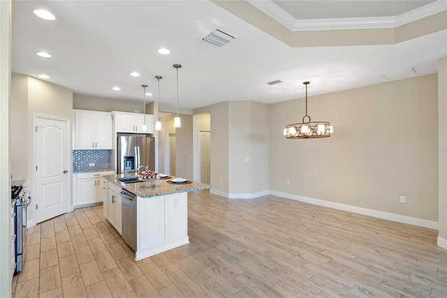 kitchen featuring light hardwood / wood-style flooring, decorative light fixtures, a center island with sink, appliances with stainless steel finishes, and ornamental molding