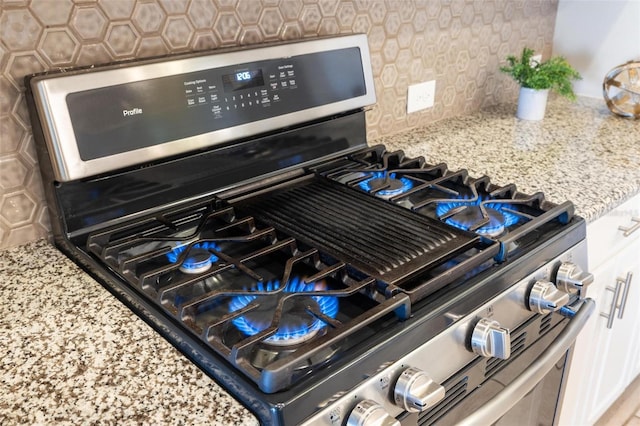 details featuring light stone counters, white cabinetry, tasteful backsplash, and gas range