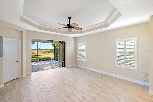 empty room with ceiling fan, a healthy amount of sunlight, a raised ceiling, and light hardwood / wood-style floors