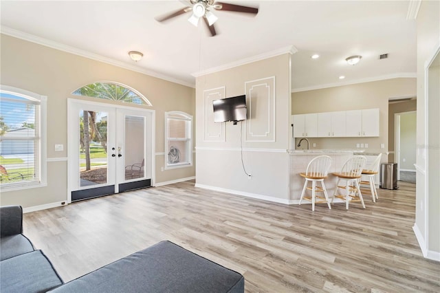 living room with ceiling fan, light wood-type flooring, ornamental molding, and french doors