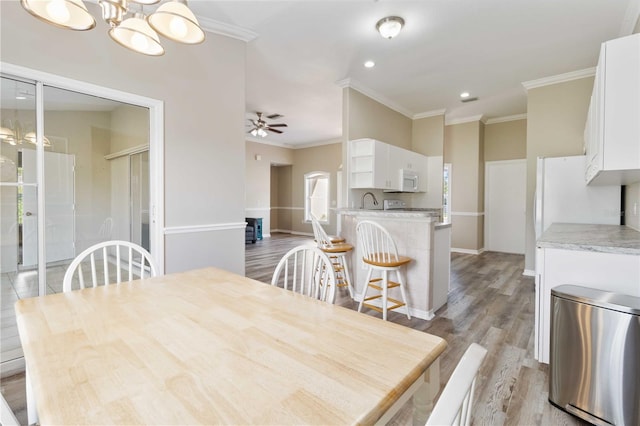 dining area featuring crown molding, light hardwood / wood-style flooring, ceiling fan with notable chandelier, and sink