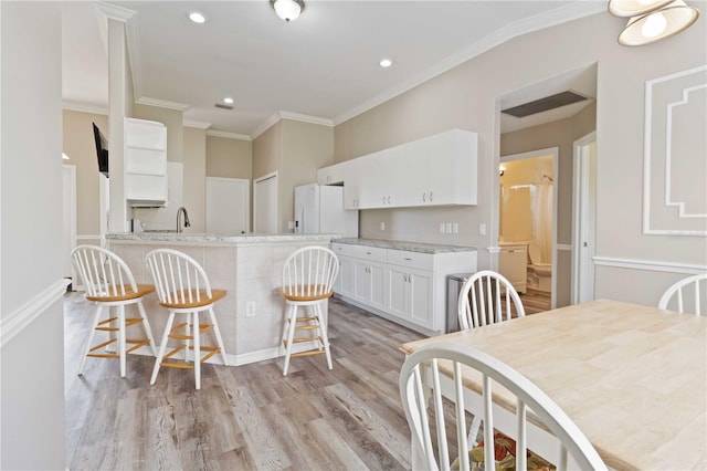 kitchen featuring white cabinets, light stone countertops, light wood-type flooring, ornamental molding, and a breakfast bar area