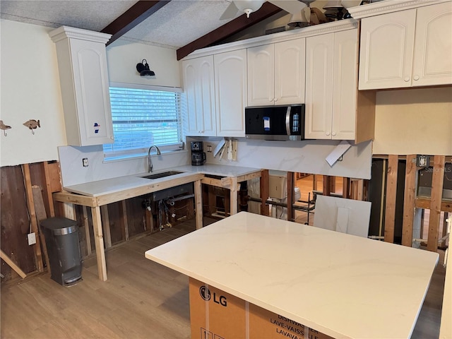 kitchen with sink, lofted ceiling with beams, light hardwood / wood-style floors, a textured ceiling, and white cabinets