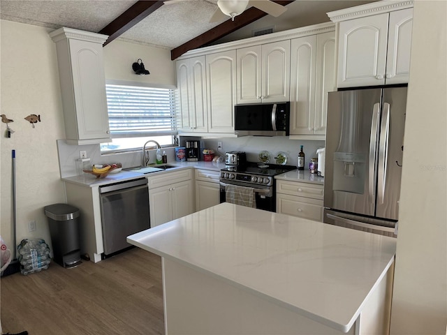 kitchen featuring a textured ceiling, stainless steel appliances, sink, vaulted ceiling with beams, and white cabinetry