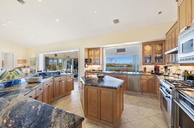 kitchen featuring lofted ceiling, dark stone countertops, light tile patterned floors, appliances with stainless steel finishes, and a kitchen island