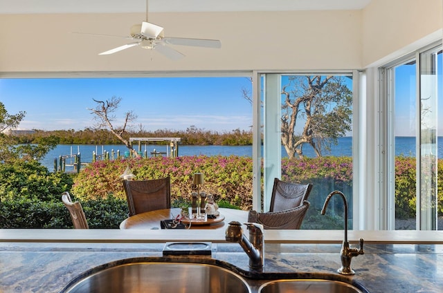 sunroom with ceiling fan and a water view