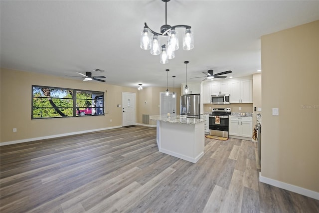 kitchen with light stone countertops, white cabinetry, stainless steel appliances, pendant lighting, and light wood-type flooring