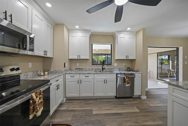 kitchen with dark wood-type flooring, white cabinets, sink, appliances with stainless steel finishes, and light stone counters