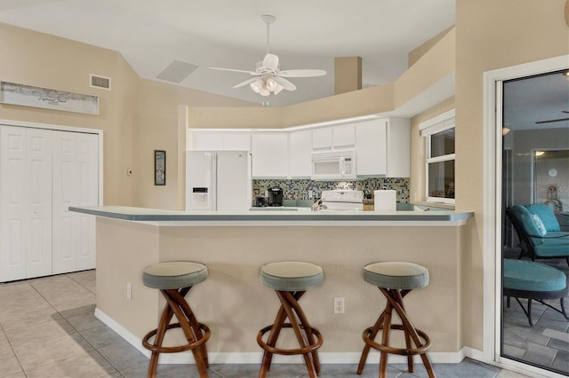 kitchen featuring white appliances, vaulted ceiling, backsplash, white cabinets, and a breakfast bar area